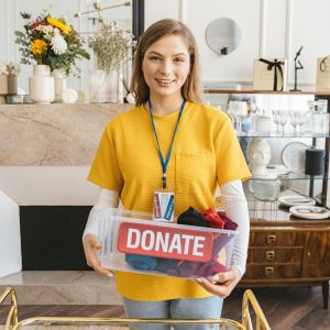 Smiling woman holding a donation box indoors, symbolizing charity and giving back to the community.