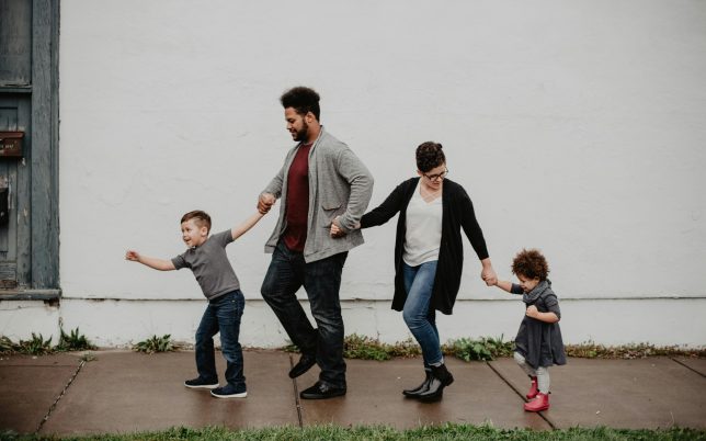 A joyful family walking together outdoors, holding hands in a playful and happy moment.