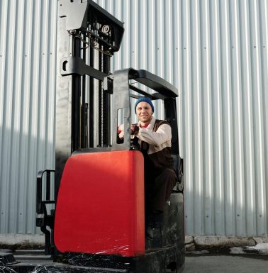 A forklift operator working outdoors in an industrial area with corrugated metal walls.
